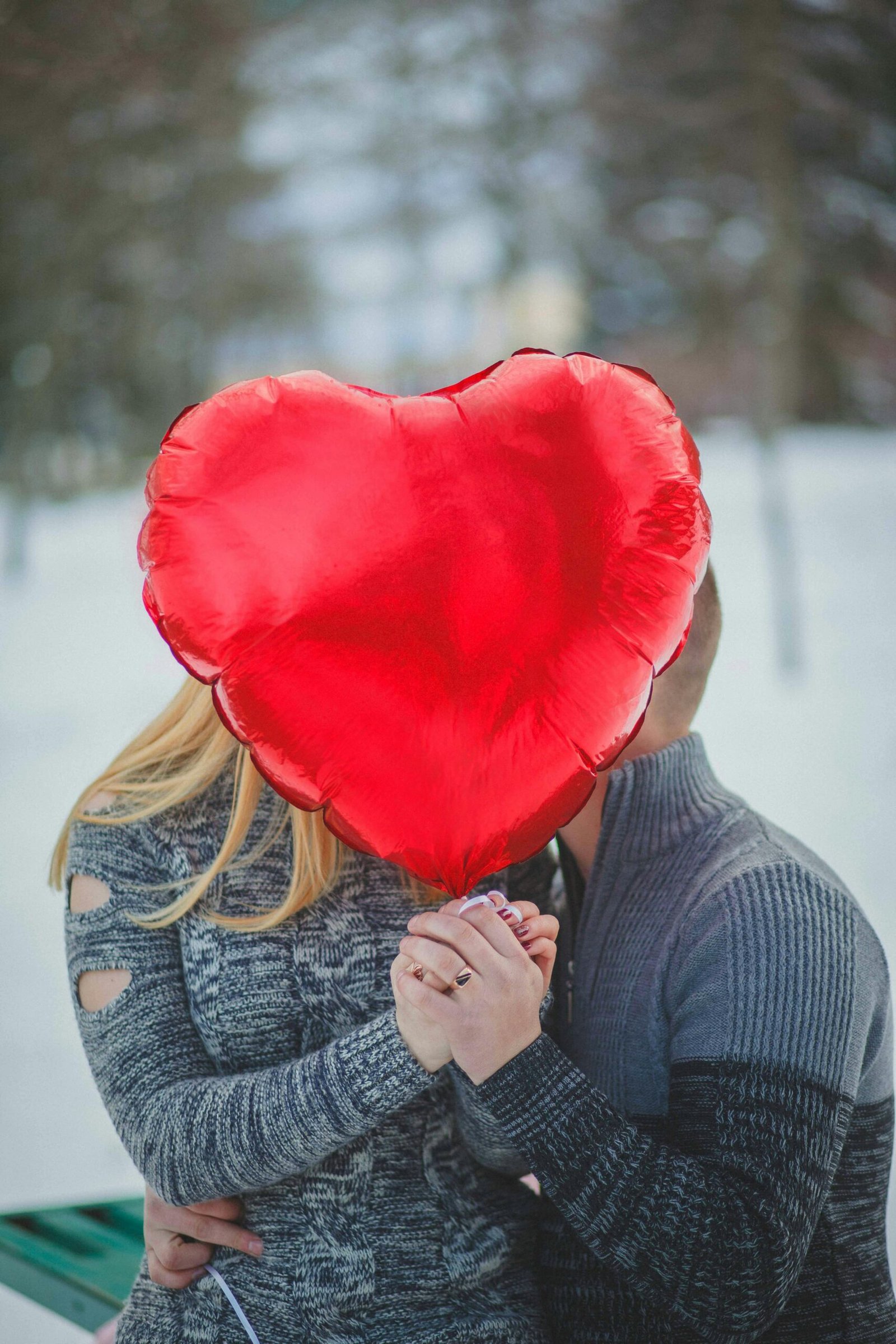 A couple embraces behind a heart-shaped balloon outdoors, depicting love and romance.